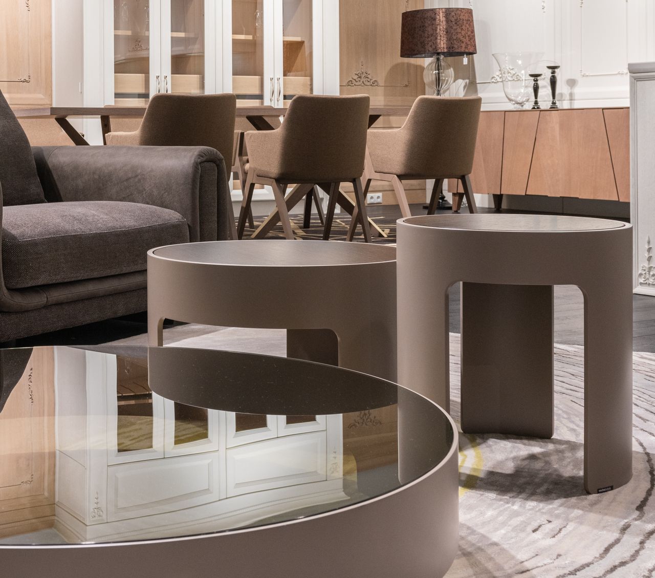 Small round tables placed near sofa and and sat of brown chairs at wooden cupboard with lamp and candlestick in modern apartment